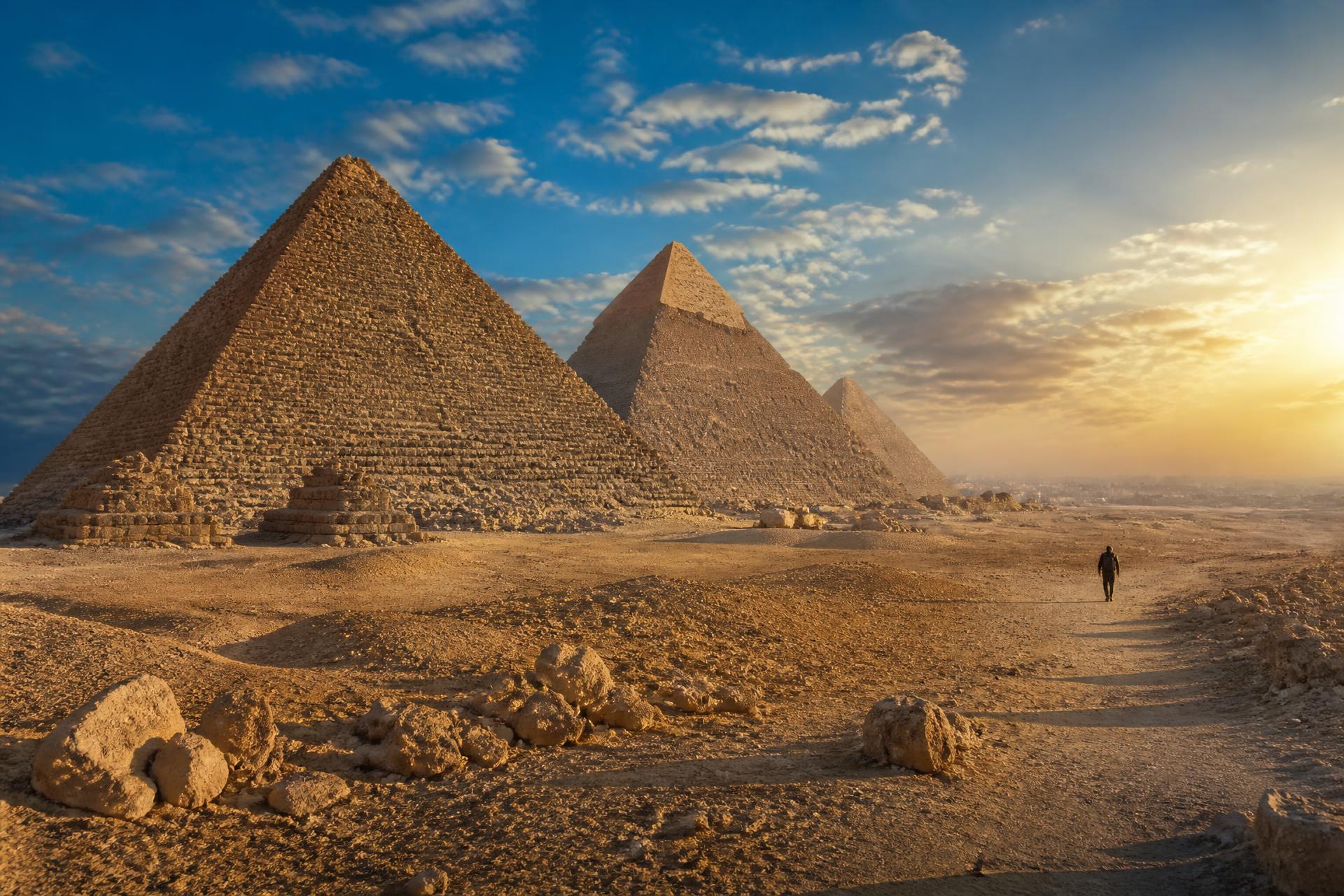 The Giza Pyramids at golden hour with a lone traveler on the desert path